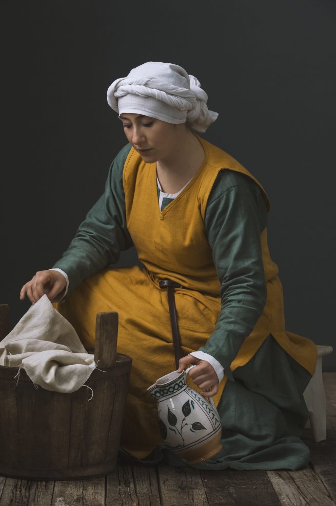 Historic portrait of a young woman in medieval clothing doing laundry. Personal project dedicated to historic portraits. Image series by David Umberto Zappa - portrait, commercial and advertising photographer. Studio photography. Set-design. Ritratto storico di giovane donna in abiti medievali intenta a lavare i panni.. Progetto personale del fotografo commerciale, pubblicitario, ritrattista ed editoriale David Umberto Zappa. Fotografia in studio. Set-design.