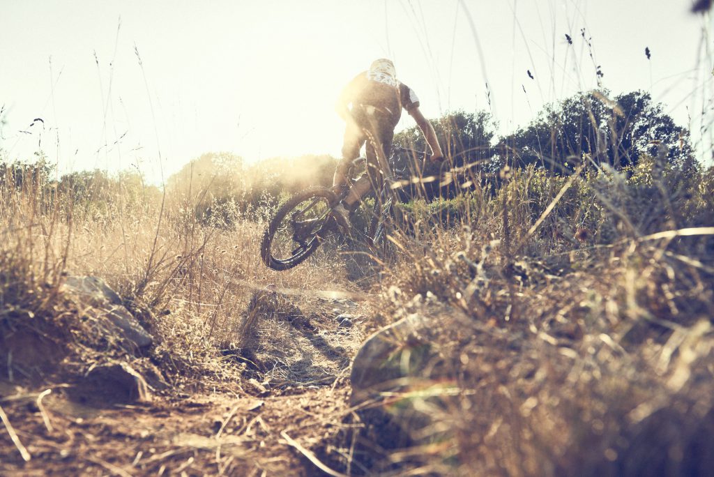 e-bike MTB. Andrea Garibbo e-bike enduro rider along the trails of Lerici under a worm summer afternoon light. Photographed at mid air through the bushes by David Umberto Zappa, portrait, commercial, editorial, sports photographer based in Italy. Andrea Garibbo, rider enduro di e-bike lungo i sentieri di Lerici avvolto dalla luce di un tardo pomeriggio estivo. Ritratto a mezz’aria dal fotografo pubblicitario, commerciale, ritrattista, sportivo David Umberto Zappa.