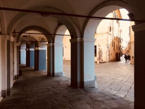 Piazza Matteotti Sarzana con facciate di palazzi storici e portici sul lato sinistro. Inferiate e portoni. Location Scout duzimage