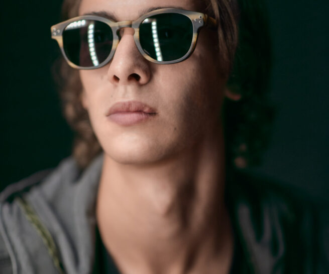 male model wearing sunglasses on a dark background with led lighting reflected on the lenses