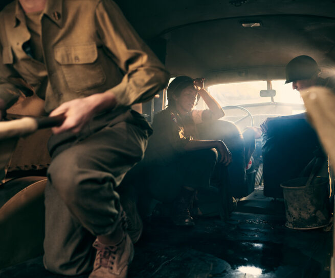 interior of a WWII ambulance with three soldiers, one of them is a woman touching her forehead lit by late afternoon warm light.