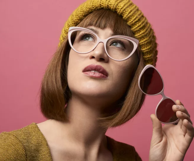 ritratto di giovane donna su sfondo rosa, con cappello color senape, mentre indossa occhiali da vista ed in mano tiene mascherina applicabile sole. Foto realizzata dal fotografo commerciale duzimage a La Spezia