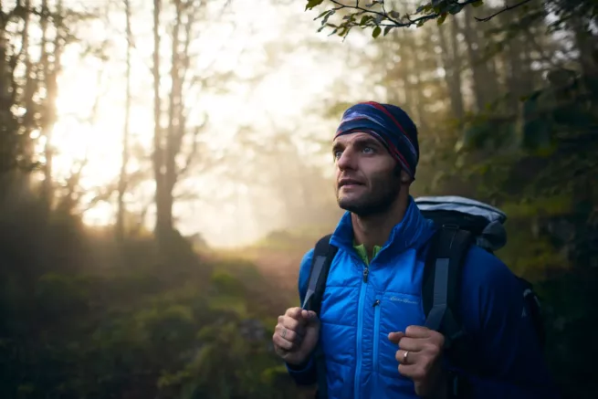 Portfolio sport & lifestyle duzimage - ritratto di uomo nel bosco con luce alle spalle e mani sullo zaino mentre guarda fuori campo