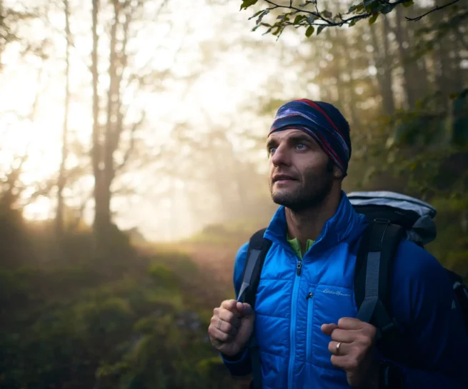 Portfolio sport & lifestyle duzimage - ritratto di uomo nel bosco con luce alle spalle e mani sullo zaino mentre guarda fuori campo